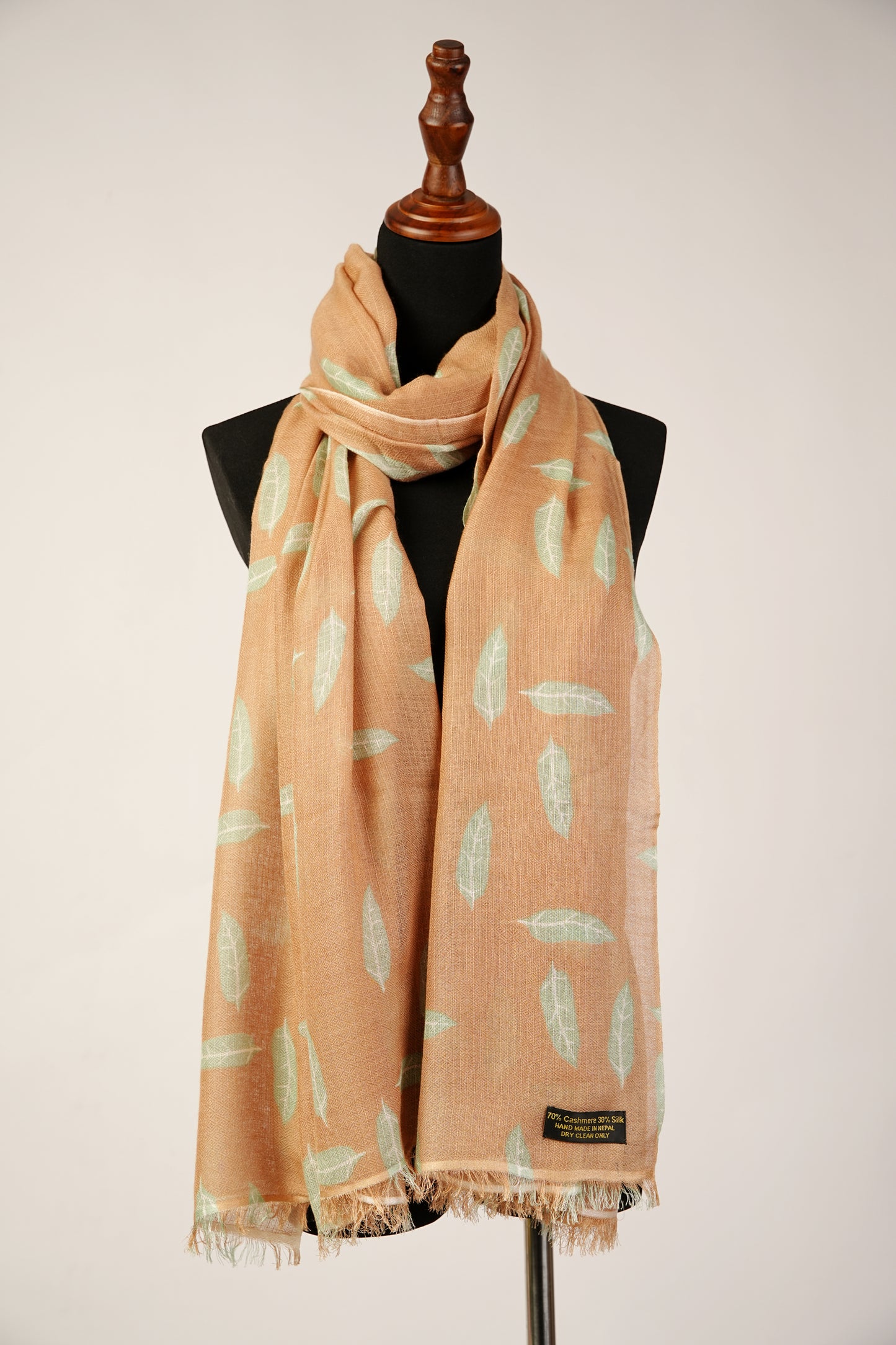 The enchanting Cashmere silk shawl features a printed image of autumn leaves gracefully descending in the cozy hues of camel brown.