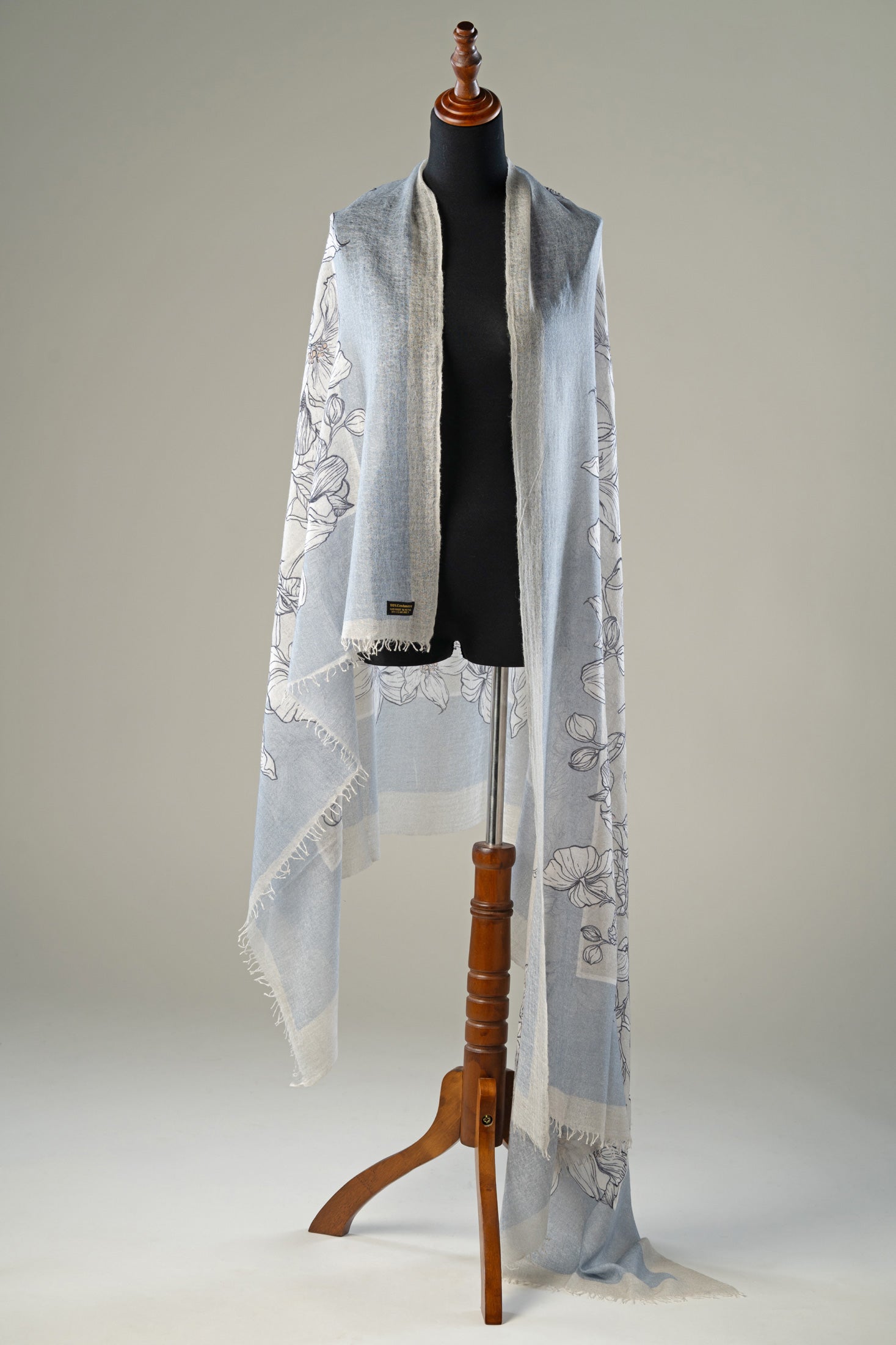 Luxury handwoven ice blue cashmere shawl featuring delicate monochrome floral illustrations and hand-fringed edges