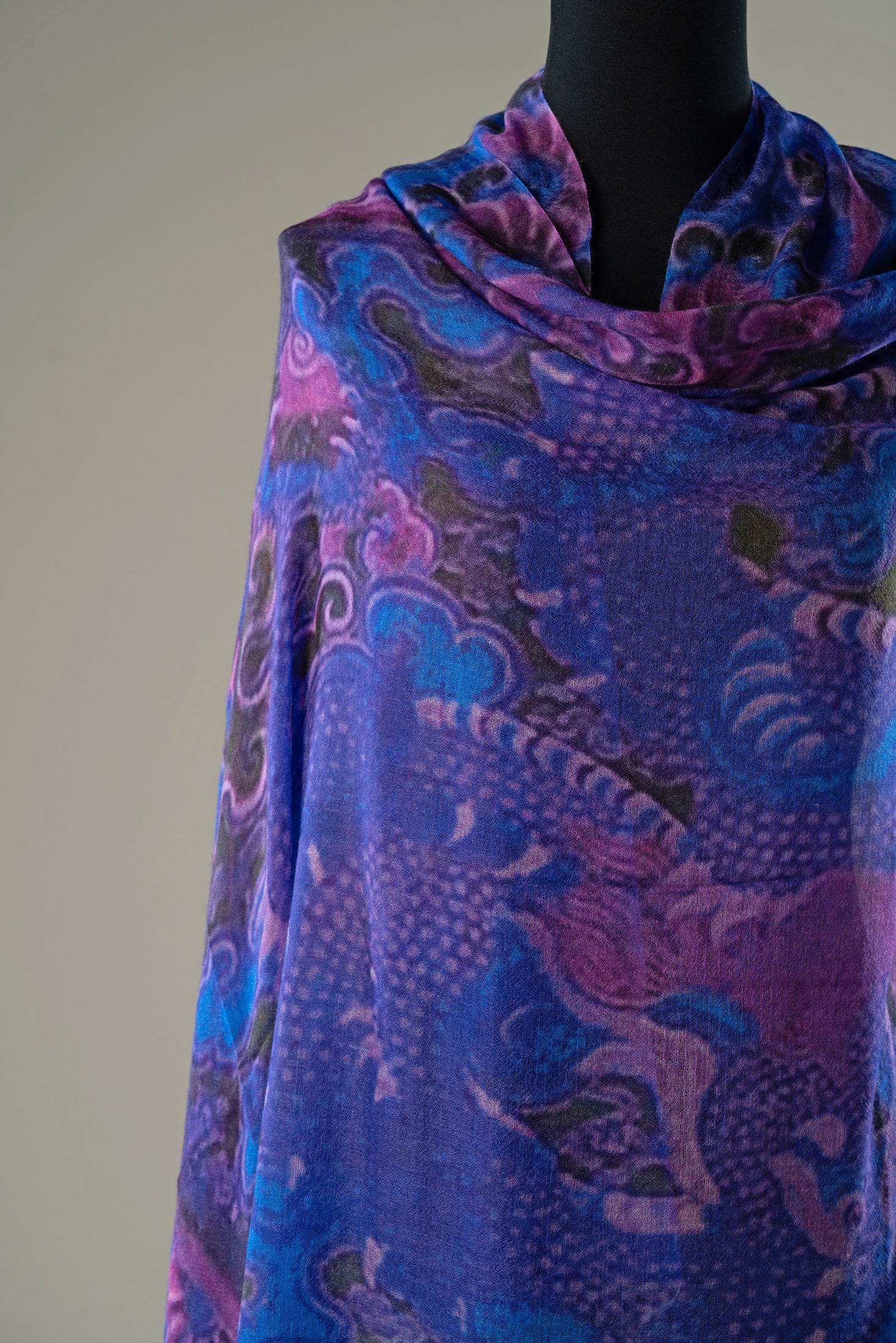 A draped scarf with a vibrant blue, purple, and pink dragon pattern, displayed on a black mannequin torso against a neutral beige background.