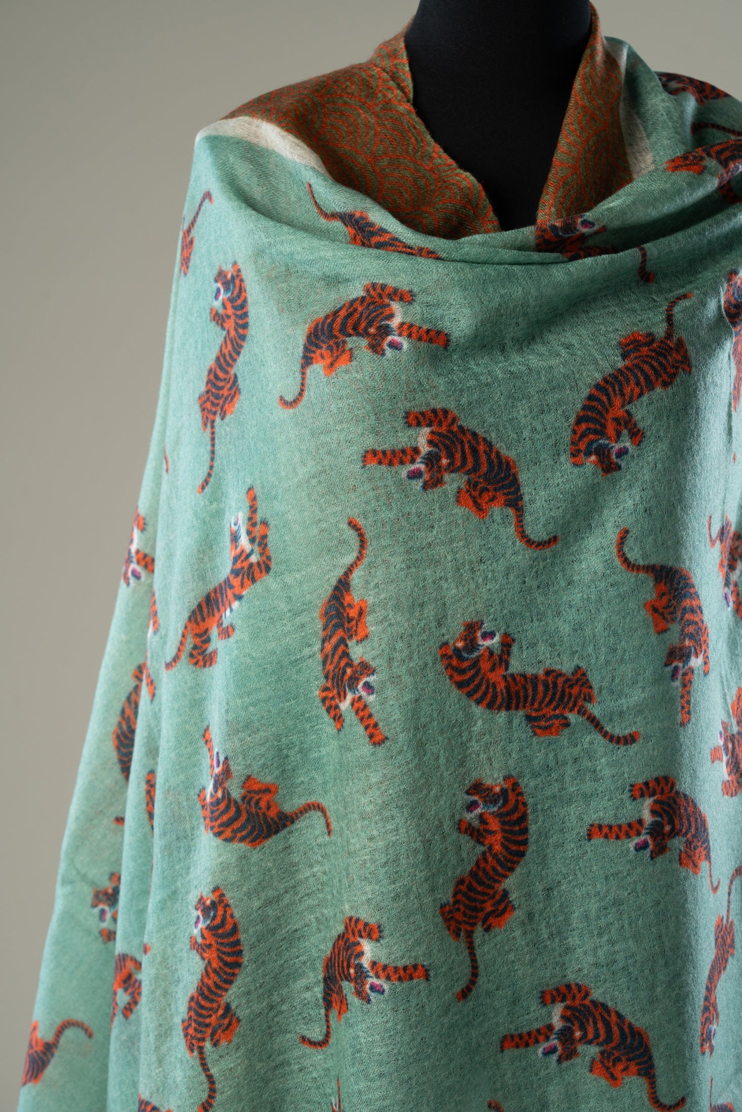 A sage green shawl with an all-over print of orange and black tigers.